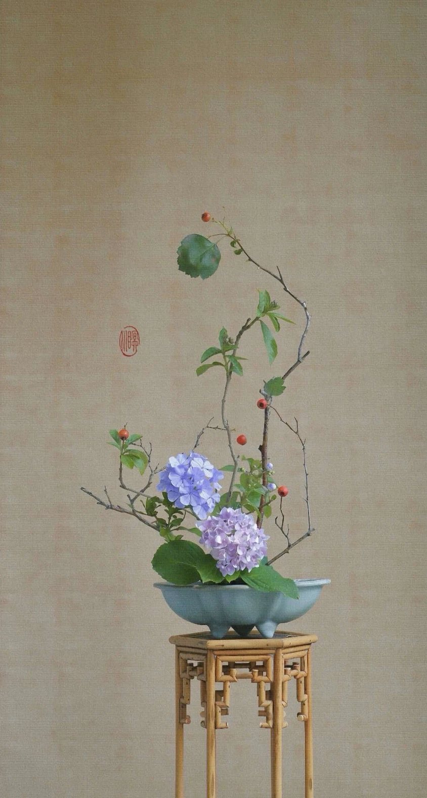 绣球与山楂枝的插花作品，置于竹制高几之上